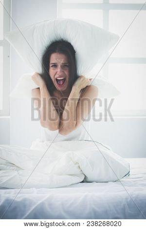 Young caucasian woman covering her head and ears with pillows
