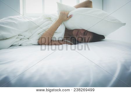 Young caucasian woman covering her head and ears with pillows