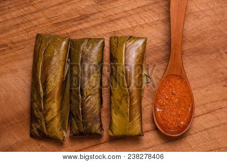 Top View Of Sticky Rice Wrapped In Leaves And Served With Peanut Sauce On Wooden Spoon. Famous Cuisi