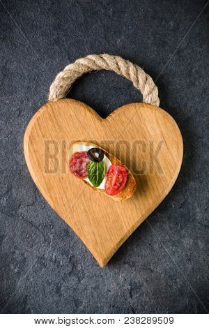 Open faced sandwich canape or crostini on a wooden serving board on dark stone  background closeup. Top view.