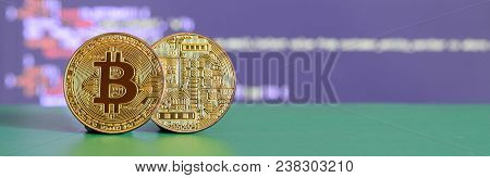 Two Gold Bitcoins Lie On The Green Surface On The Background Of The Display, Which Shows The Process