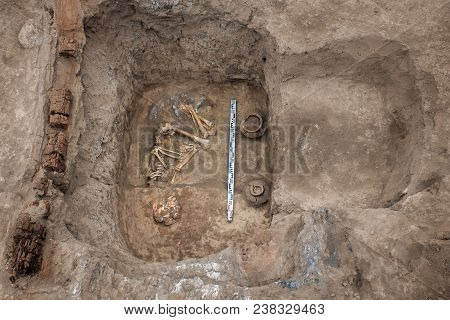 Archaeological Excavations. Top View Of The Burial Of A Person, Bones, Skull With Two Ritual Ceramic