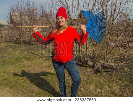 Full Length Portrait Of A Smiling Woman Professional Gardener With A Rake, A Beautiful Blonde Workin