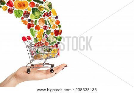 Female Hand Holding Grocery Cart With Vegetables And Fruits Falling In It Isolated On White. Healthy