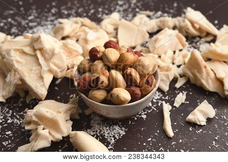 White Broken Chocolate Pieces On Dark Background, Coconut Powder And Hezelnuts In Bowl, Closeup. Swe