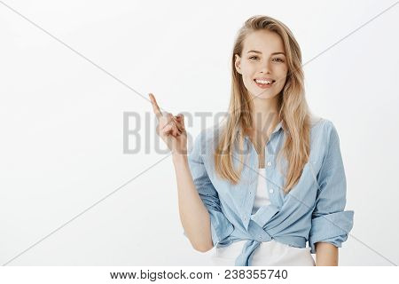 Indoor Shot Of Creative Stylish Blond Woman With Broad Smile, Raising Index Finger While Pointing At