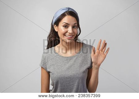 Studio Shot Of Gorgeous Beautiful Girl In Her Twenties Posing Against Blank Gray Wall, Wearing Headb