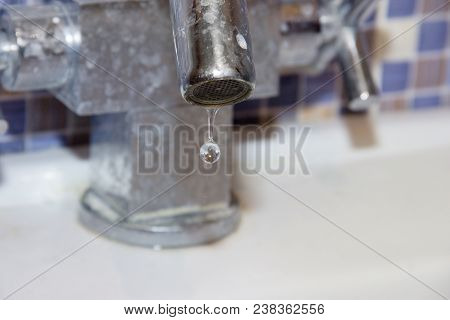 Close-up Of Leakage Tap. A Huge Drop Of Water Falls From The Tap Covered With A Calcareous Coating. 