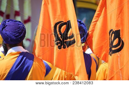 Symbol Of The Sikh Religion Called Khanda Formed By Two Scimitars On The Orange Flags And The Man Wi