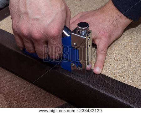 Two Man Hands Using Stapler And Staples Upholstering Paricle Board With Leatherette. Close-up