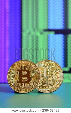 Two Gold Bitcoins Lie On The Green Surface On The Background Of The Display, Which Shows The Process