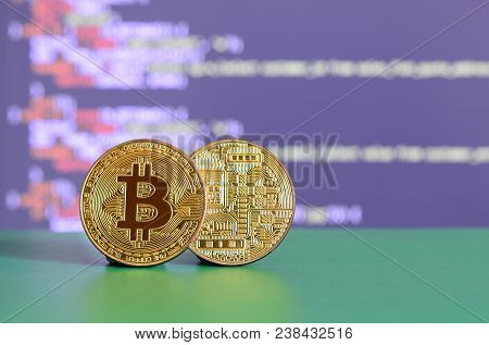 Two Gold Bitcoins Lie On The Green Surface On The Background Of The Display, Which Shows The Process