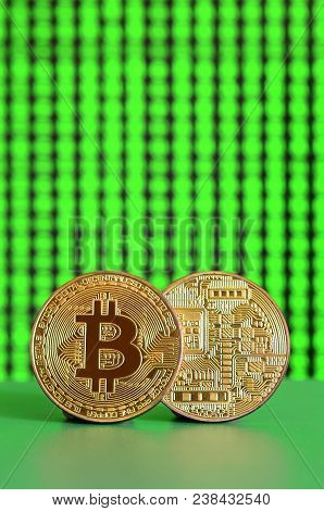 Two Gold Bitcoins Lie On The Green Surface On The Background Of The Display, Which Shows The Process