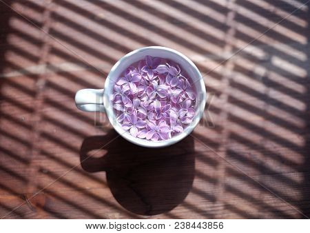 White Cup Full Of Lilac Flowers In Over Blinds Shadow Texture.