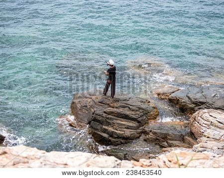 Fisherman Stands On A Rock At The Coast Fishing