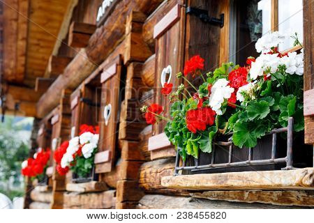 Typical Bavarian Or Austrian Wooden Window With Red Geranium Flowers On House In Austria Or Germany.
