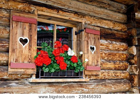 Typical Bavarian Or Austrian Wooden Window With Red Geranium Flowers On House In Austria Or Germany.