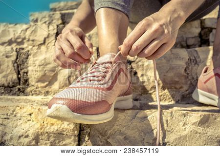 Women runner bootlace on her boot after running in sunny day under sunlight from blue sky on the stone steps.