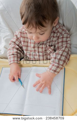 Little baby boy is playing with pen and note book