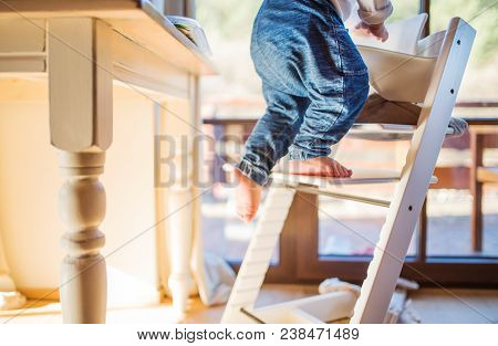 Little Toddler Boy Climbing On Wooden Highchair At Home. Domestic Accident. Dangerous Situation At H
