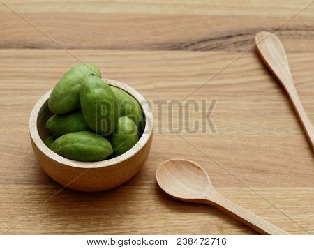 A Group Of Green Hog Plums Fruit In Wooden Bowl With Wooden Spoon Over Bright Wooden Background With