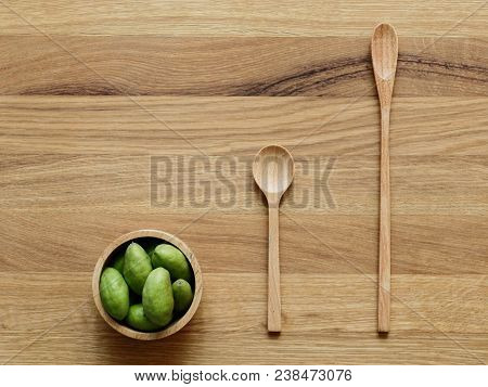 A Group Of Green Hog Plums Fruit In Wooden Bowl With Wooden Spoon Over Bright Wooden Background With