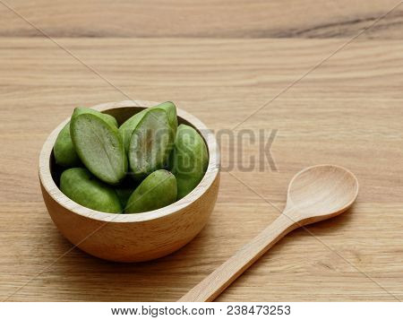 A Group Of Green Hog Plums Fruit In Wooden Bowl With Wooden Spoon Over Bright Wooden Background With