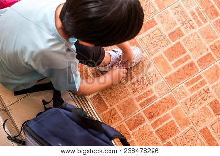 A Boy Is Tying The Shoelaces To Prepare To Go To School In The Morning At Home Hastily. Copy Space F