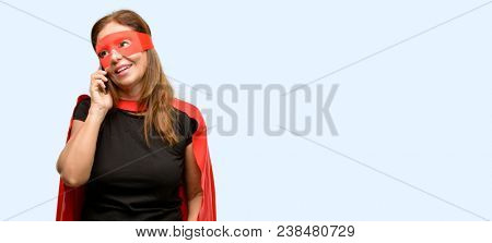 Middle age super hero woman wearing red mask and cape happy talking using a smartphone mobile phone isolated blue background