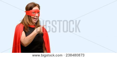Middle age super hero woman wearing red mask and cape pointing away side with finger isolated blue background