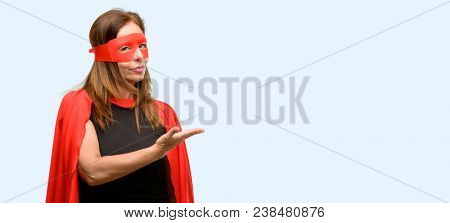 Middle age super hero woman wearing red mask and cape holding something in empty hand isolated blue background