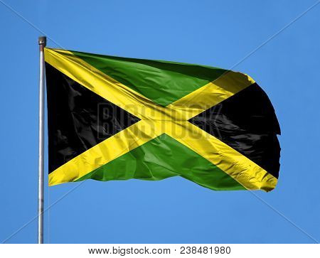 National Flag Of Jamaica On A Flagpole In Front Of Blue Sky.