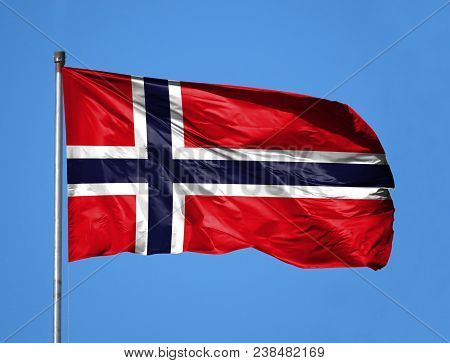 National Flag Of Norway On A Flagpole In Front Of Blue Sky.