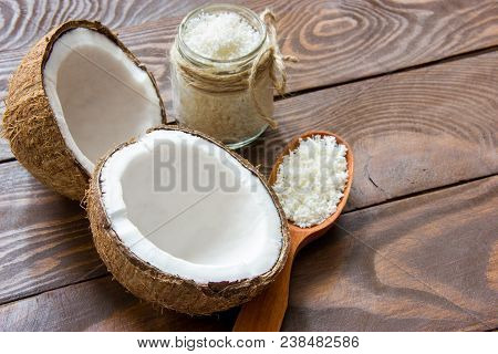 Two Halves Of Coconut Lie On A Wooden Table Shavings In A Glass Jar And A Wooden Spoon