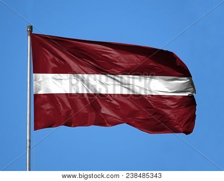 National Flag Of Latvia On A Flagpole In Front Of Blue Sky.