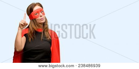 Middle age super hero woman wearing red mask and cape happy and surprised cheering expressing wow gesture pointing up isolated blue background