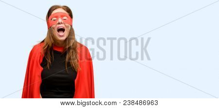 Middle age super hero woman wearing red mask and cape stressful, terrified in panic, shouting exasperated and frustrated. Unpleasant gesture. Annoying work drives me crazy isolated blue background