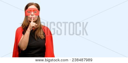 Middle age super hero woman wearing red mask and cape with index finger on lips, ask to be quiet. Silence and secret concept isolated blue background