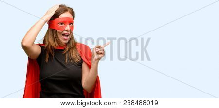 Middle age super hero woman wearing red mask and cape pointing away side with finger isolated blue background