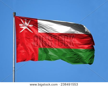 National Flag Of Oman On A Flagpole In Front Of Blue Sky.