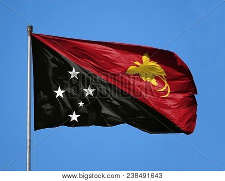 National Flag Of Papua New Guinea On A Flagpole In Front Of Blue Sky.