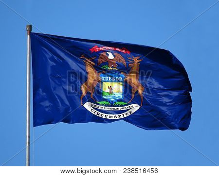 National Flag State Of Michigan On A Flagpole In Front Of Blue Sky.