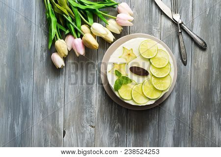 Appetizing Cake With Slices Of Lime And Mint With Tulips On A Wooden Gray Background, Top View