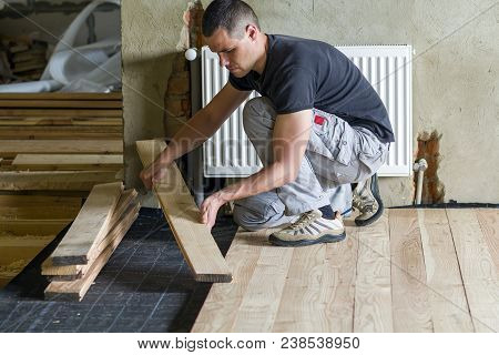 Young Handsome Professional Carpenter Installing Natural Wooden Planks On Wooden Frame Floor In Empt
