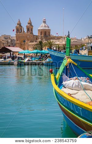 Traditional Colourful Maltese Luzzu Fishing Boats In The Turquoise Blue Water Of Marsaxlokk Harbour,