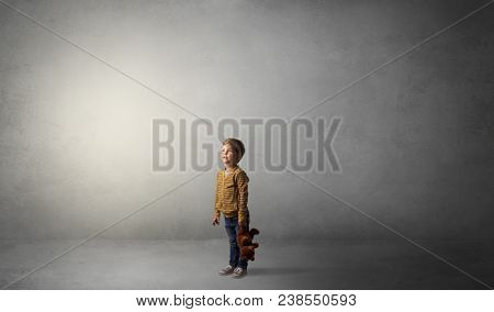 Little waggish kid staying alone in a big empty room with his plush
