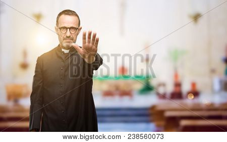 Priest religion man annoyed with bad attitude making stop sign with hand, saying no, expressing security, defense or restriction, maybe pushing at church