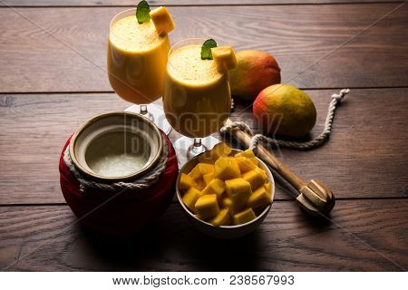 Mango Lassi Or Smoothie In Big Glass Or Small Bottles With Curd, Cut Fruit Pieces And Blender. Moody