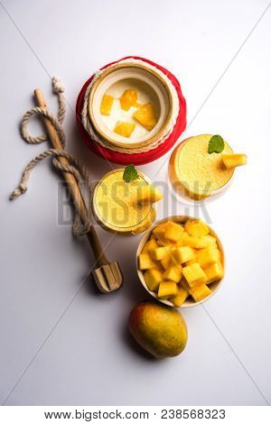 Mango Lassi Or Smoothie In Big Glass Or Small Bottles With Curd, Cut Fruit Pieces And Blender. Moody
