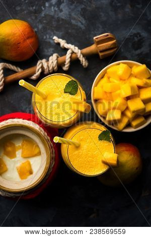 Mango Lassi Or Smoothie In Big Glass Or Small Bottles With Curd, Cut Fruit Pieces And Blender. Moody